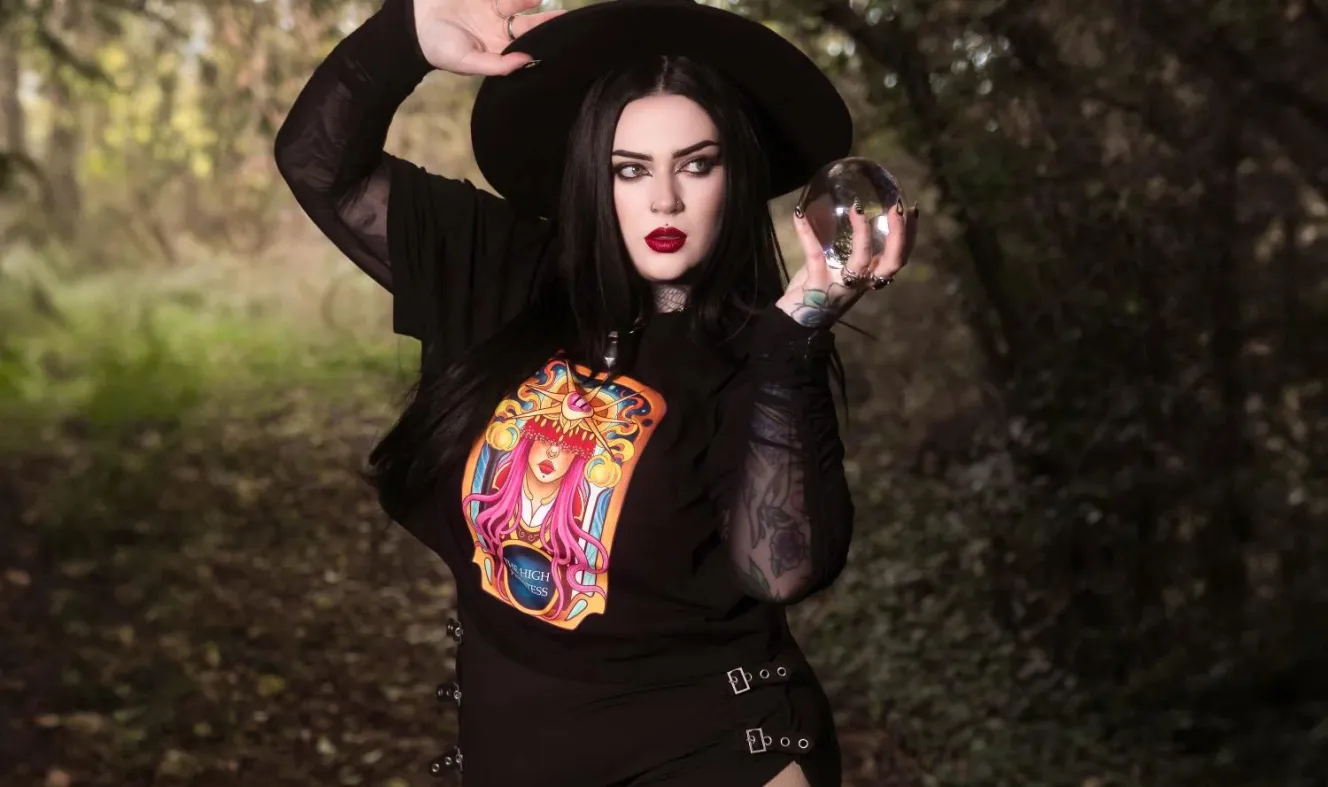 A woman wearing a black High Priestess Boxy Tee and black Snag Tights with a flowing skirt, holding a crystal ball.