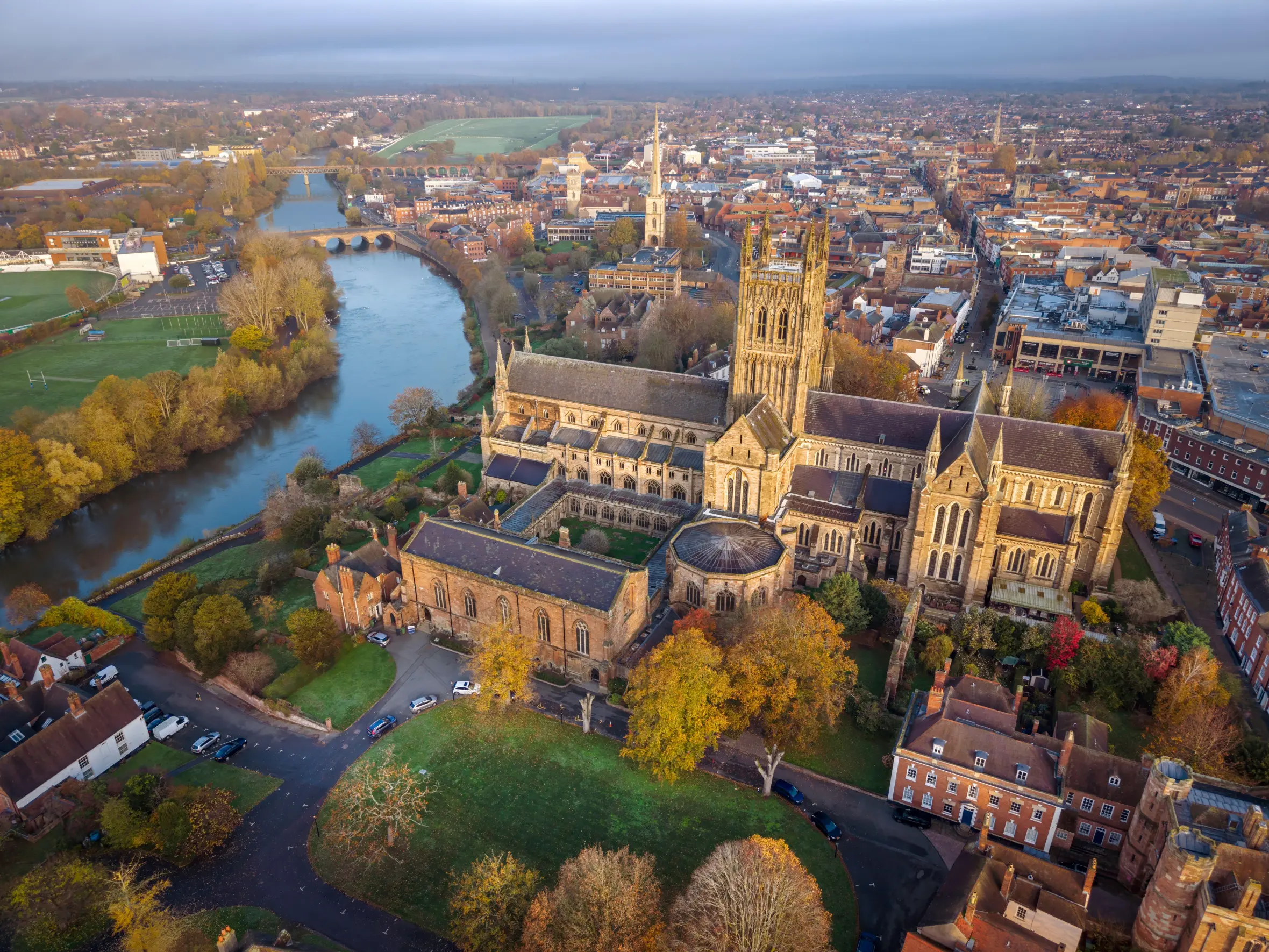 Aerial view of Worcester Cathedral and the city along the River Severn in autumn sunlight.