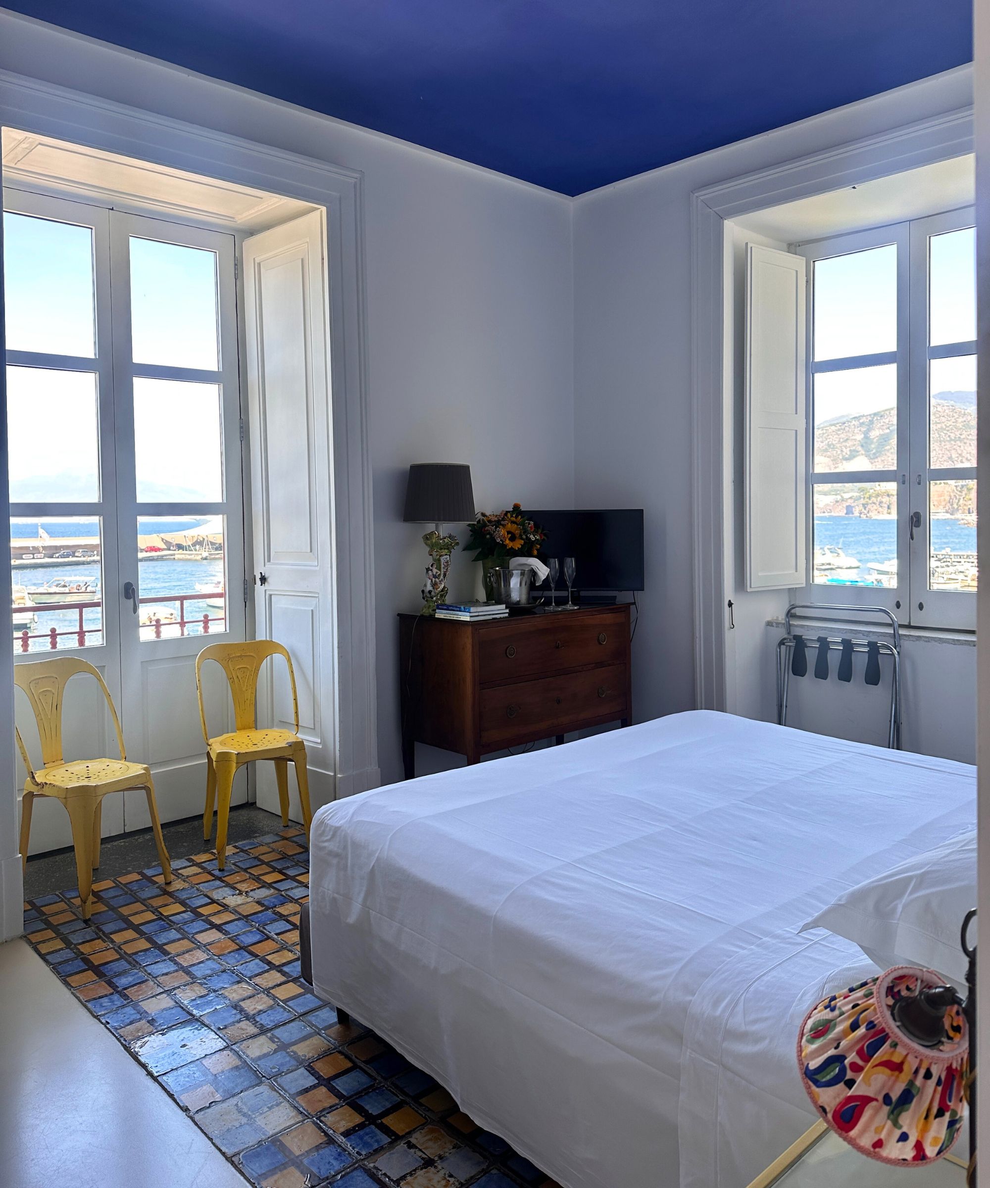 A white hotel room at marina piccola 73 in positano, Italy with a blue painted ceiling and yellow metal chairs.