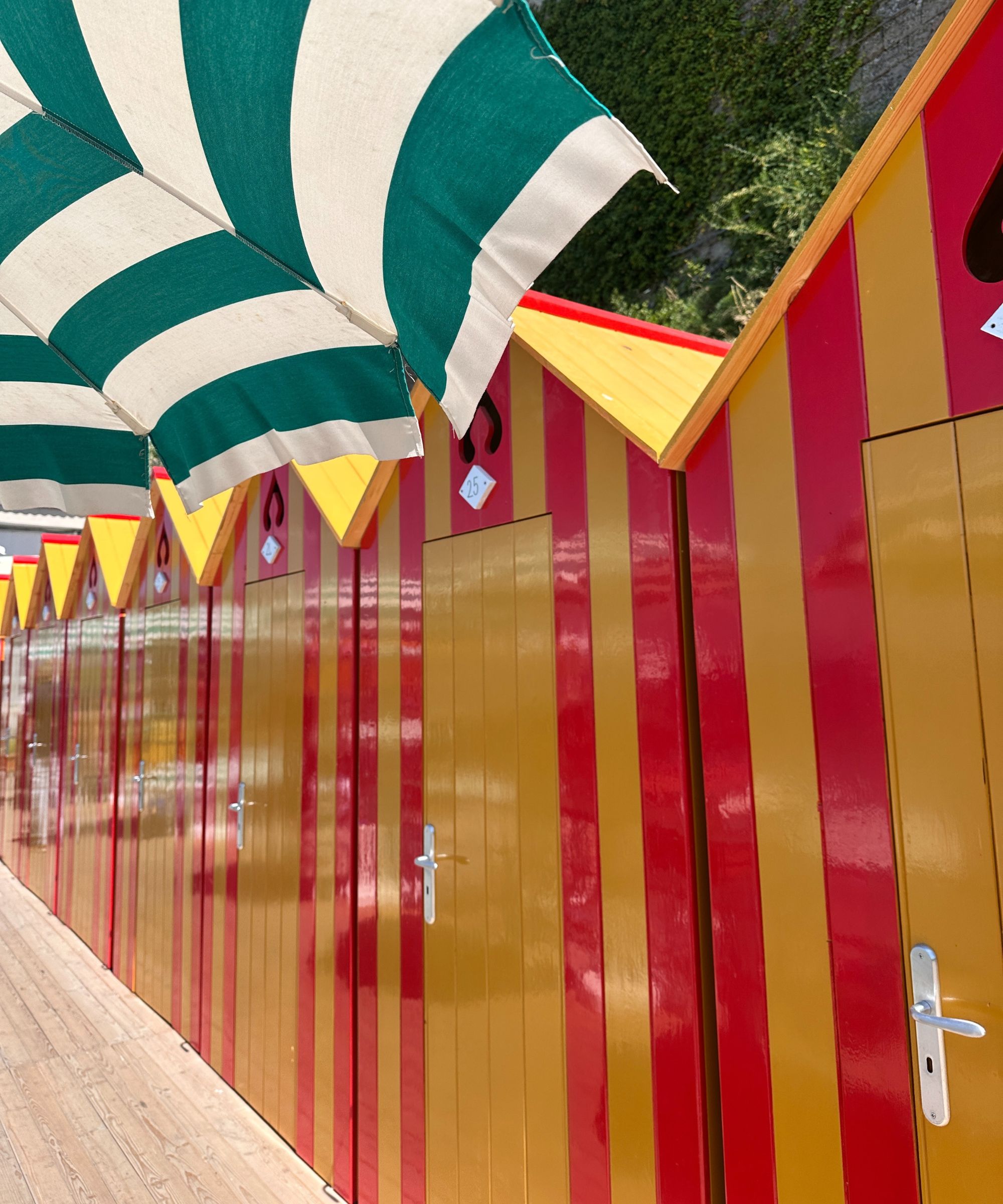 red and yellow beach huts in positano, italy with a green and white striped umbrella.
