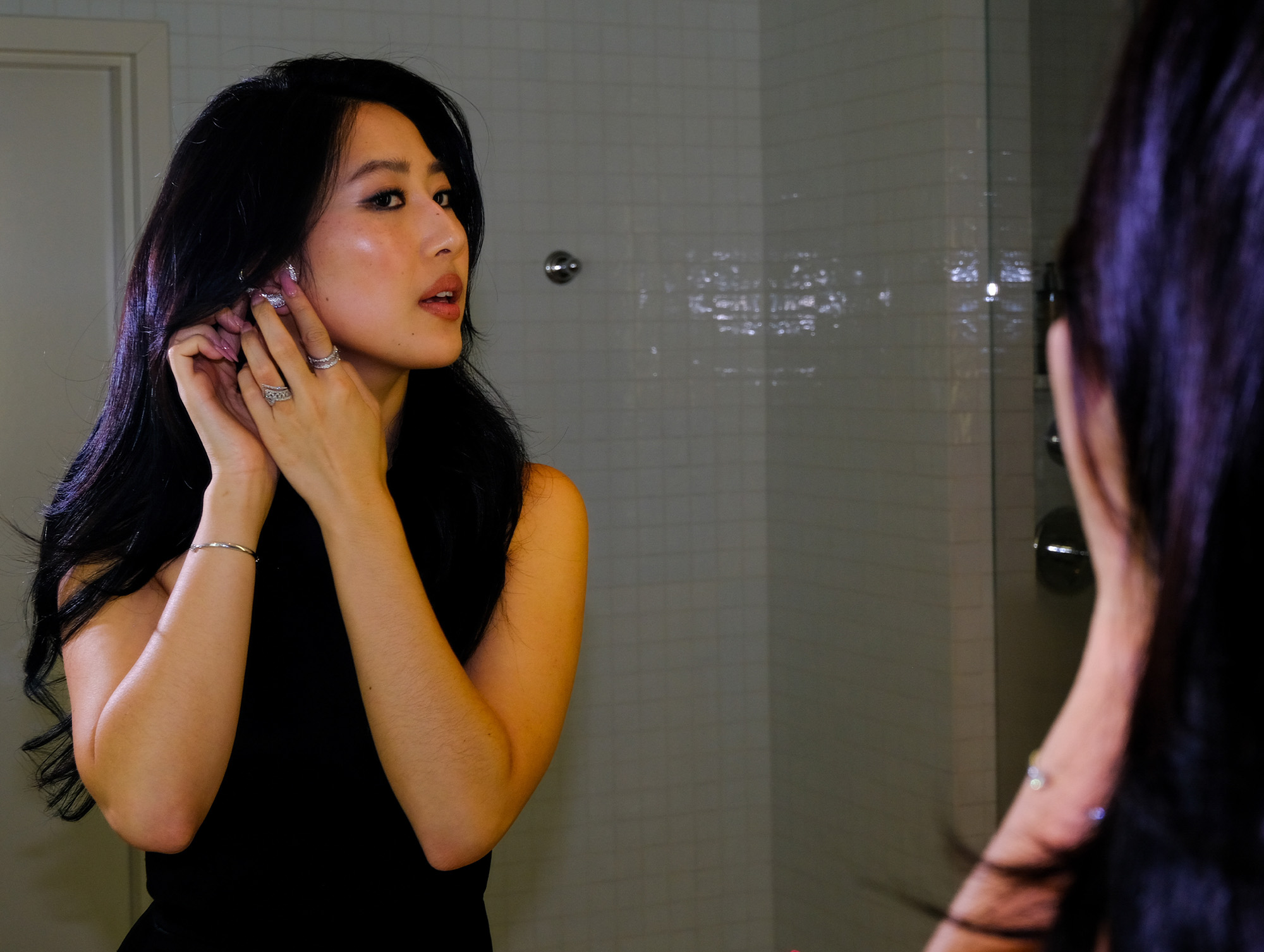 Actress Mabel Li was photographed getting ready for the premiere of The Testaments in LA. She is looking in the mirror adjusting her earrings.