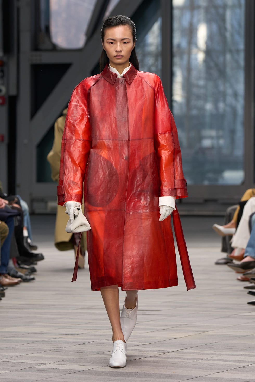 A model walking the runway is wearing a red trench coat.