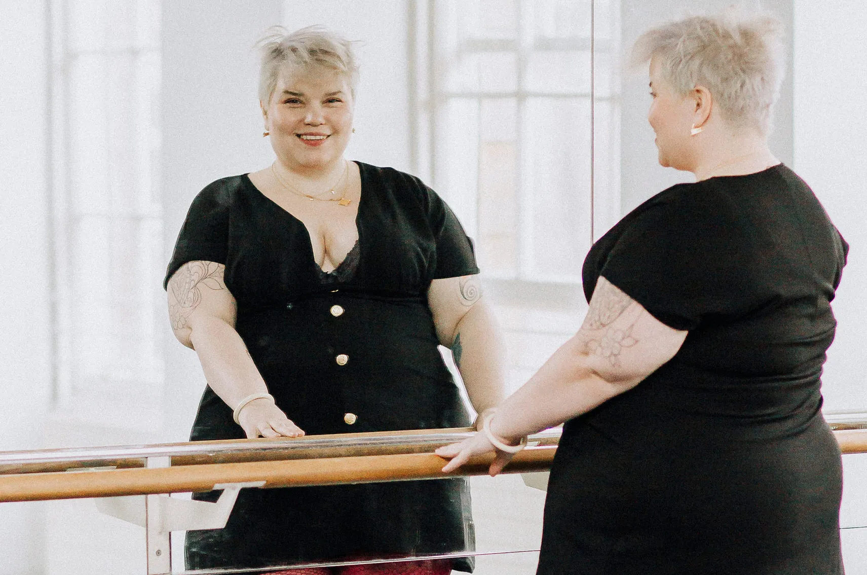 Brie Read, CEO of Snag Clothing, wearing a black dress and red tights, smiles in front of the mirror.