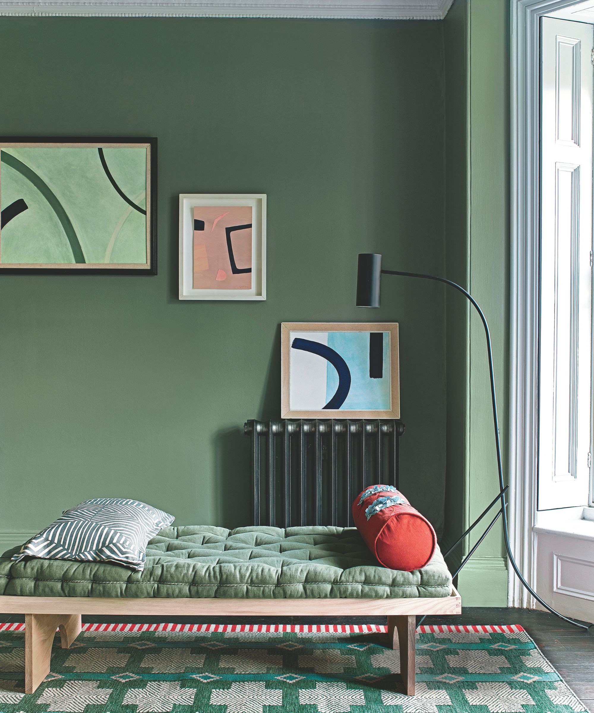 A green living room with a sunbed and three abstract paintings hung in a row