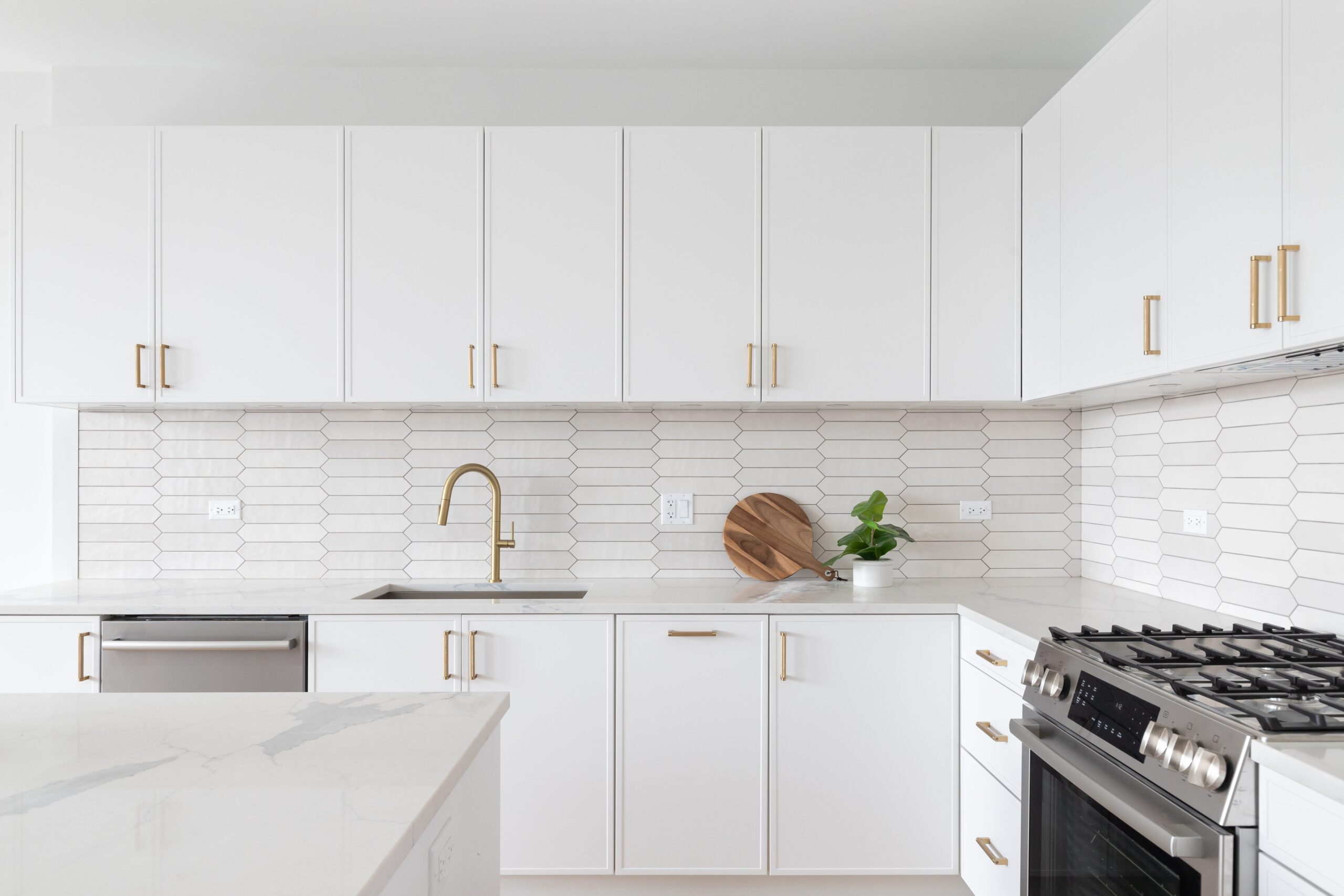White kitchen with gold faucet and hardware and brown tile picket backsplash.