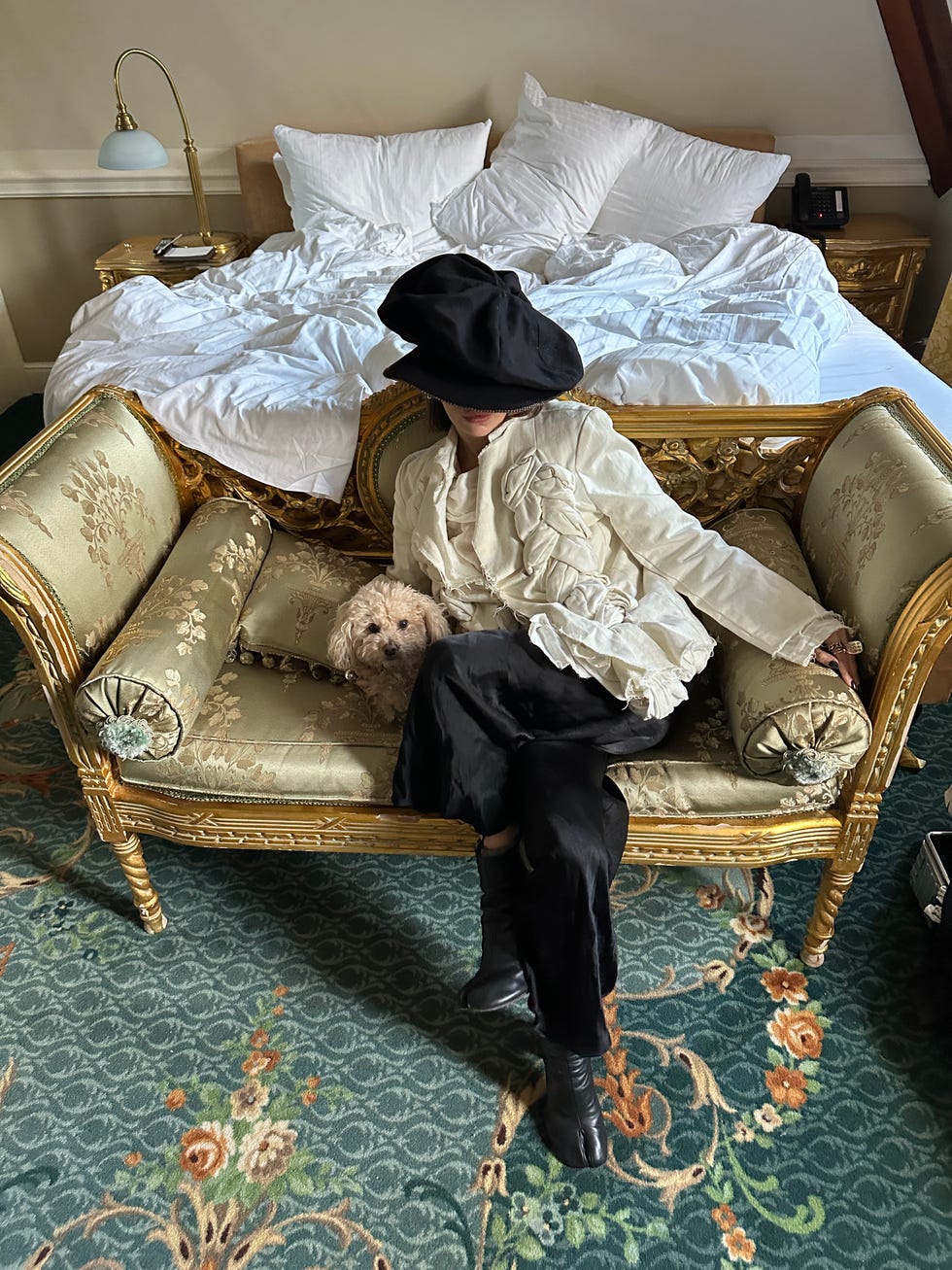 A person sitting on an old sofa with a small dog in a luxurious room.