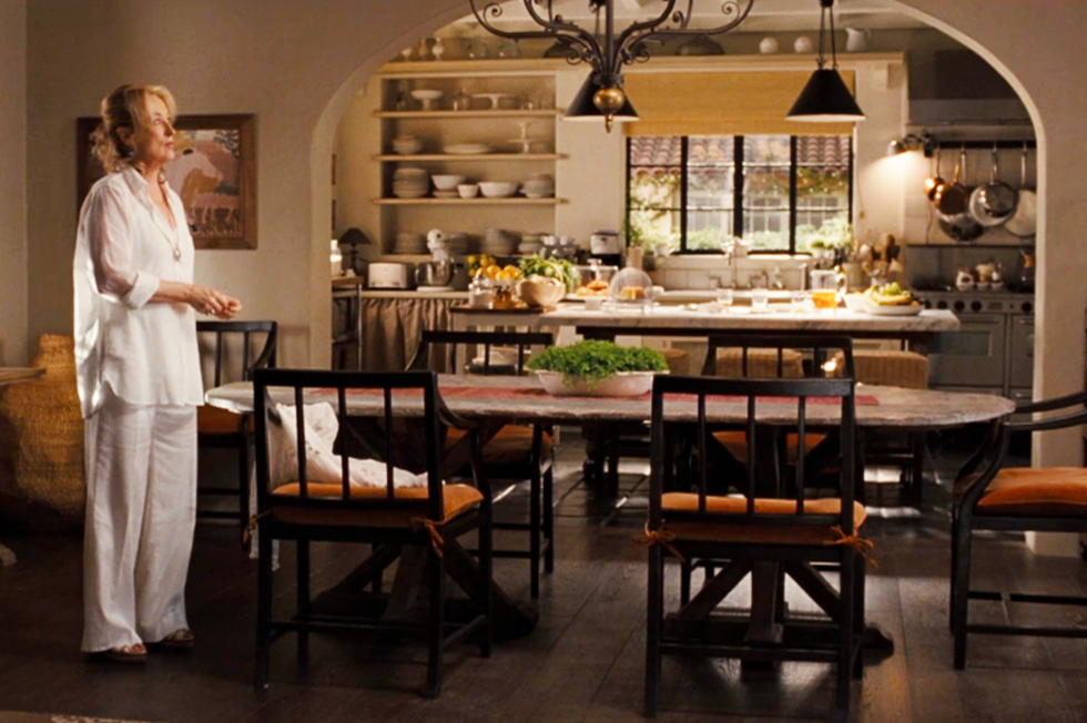 a cozy kitchendining area with a woman in a casual white dress surrounded by wooden furniture and natural light