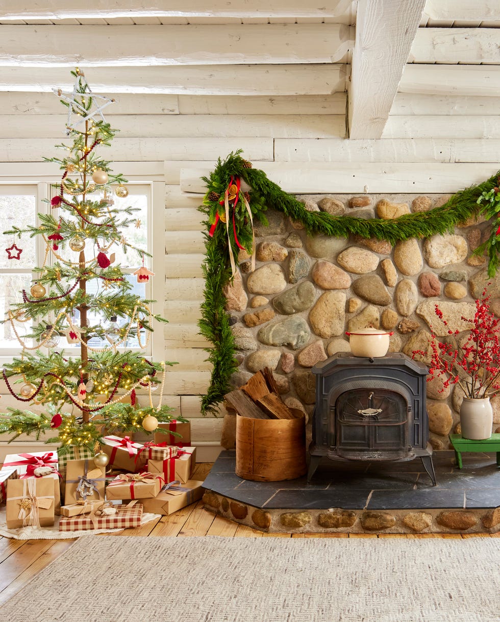 A log cabin living room painted all white with a wispy Christmas tree and wood burning stove