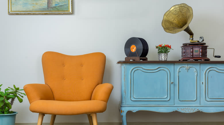Retro living room display, yellow chair and blue console table pushed to the wall; old record player and records above.