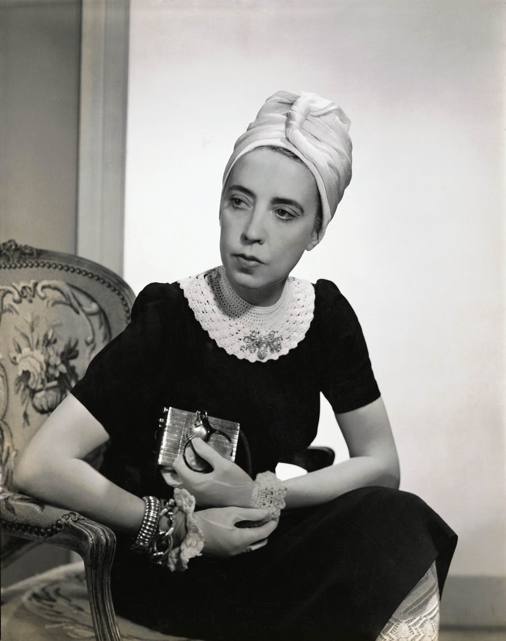 Designer Elsa Schiaparelli wears a black silk dress with a woven neckline of her own design and a tuban, as featured in Vogue in 1940.